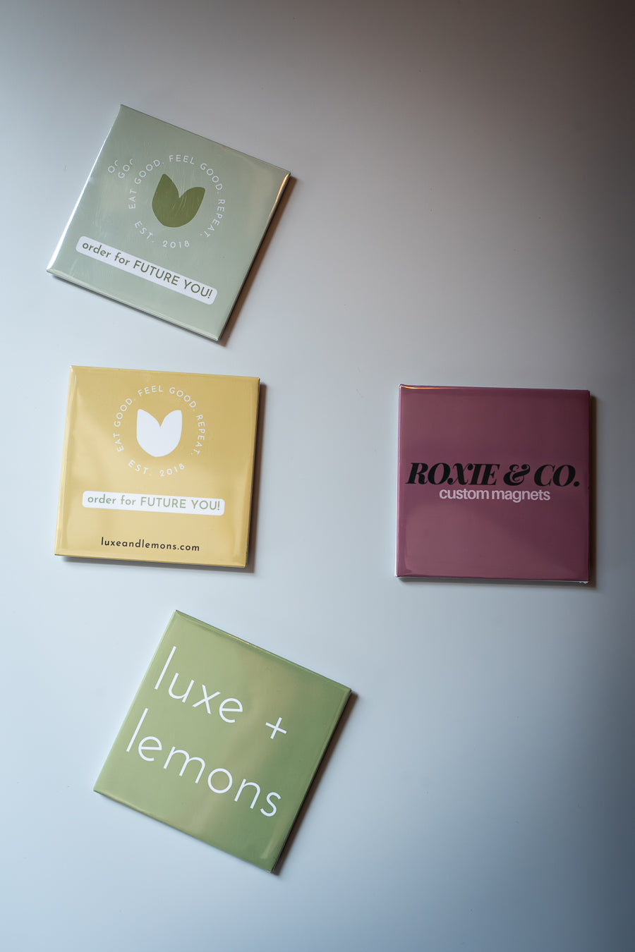 Four square magnets with different designs and text on a light gray background